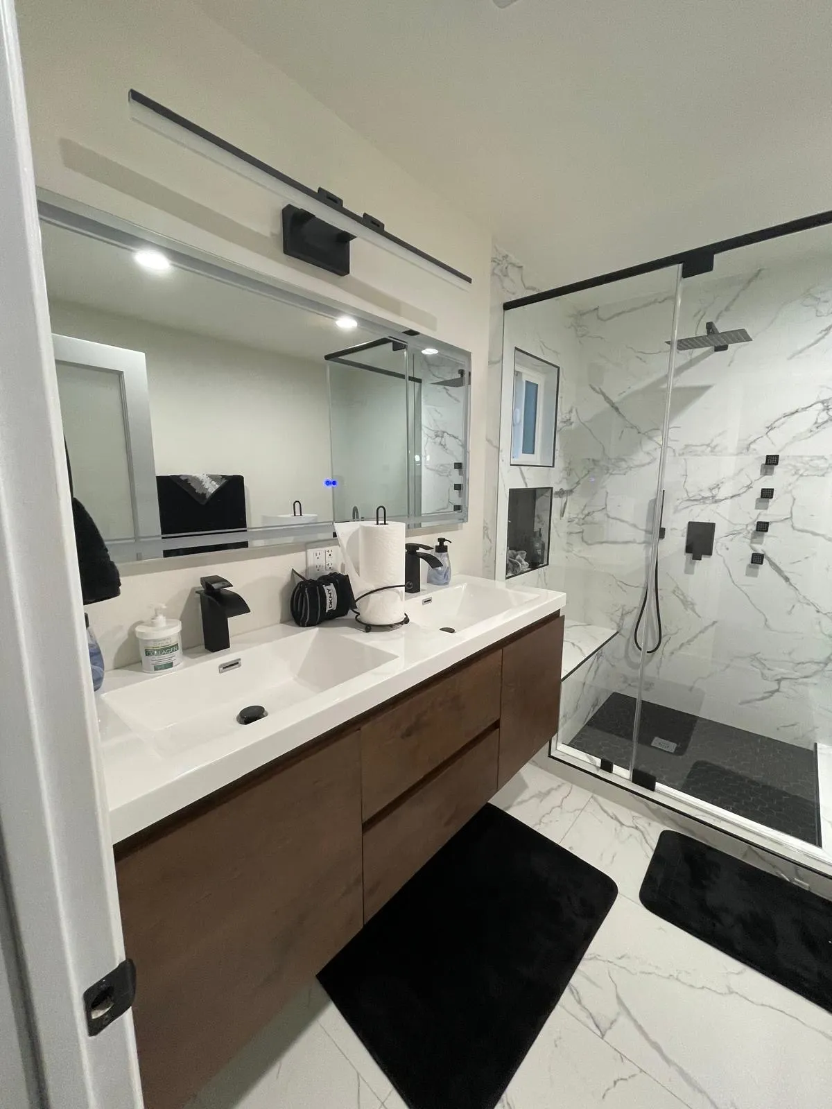 Bathroom with double vanity, lit mirror and marble-look glass shower