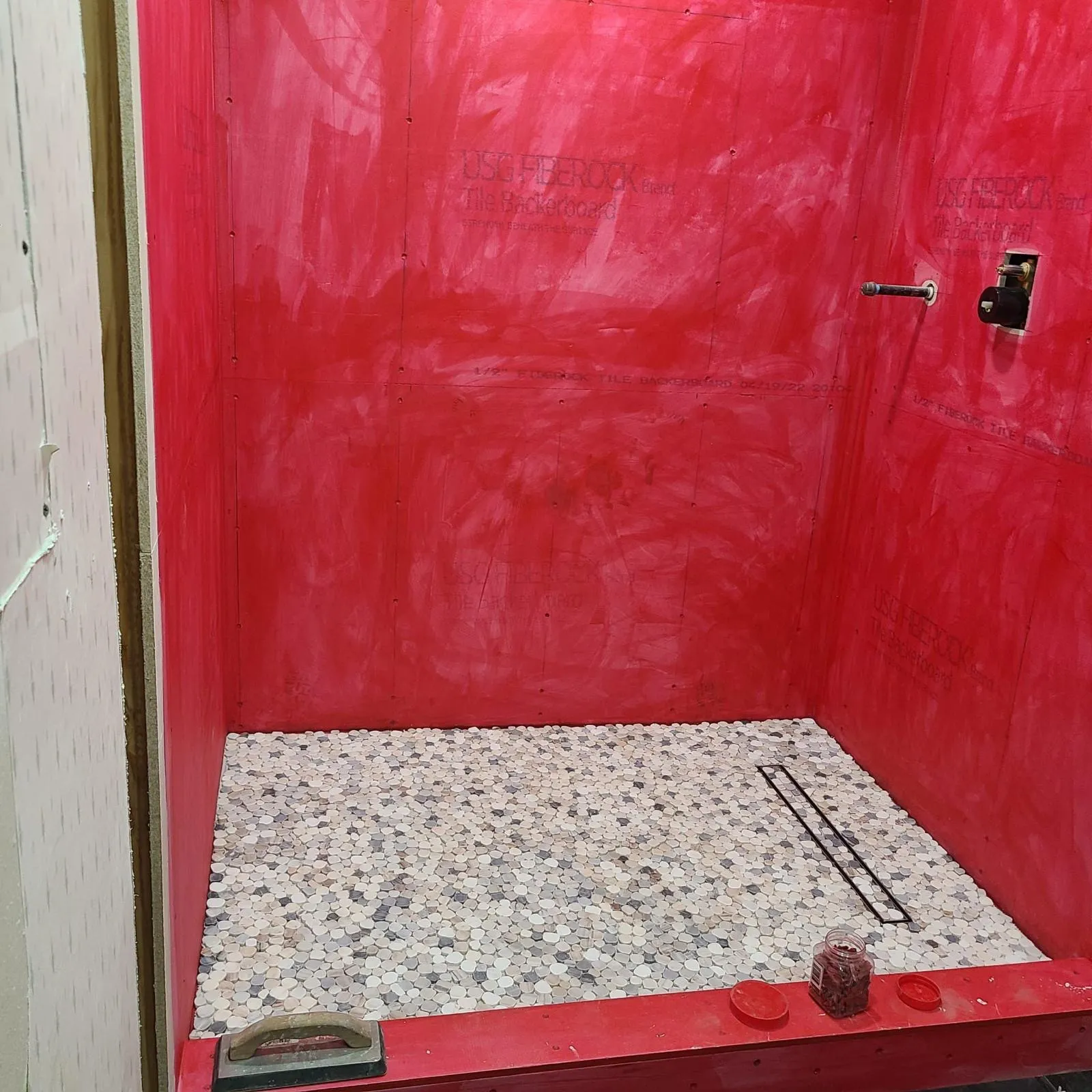 Waterproofed shower with pebble floor and linear drain before wall tile