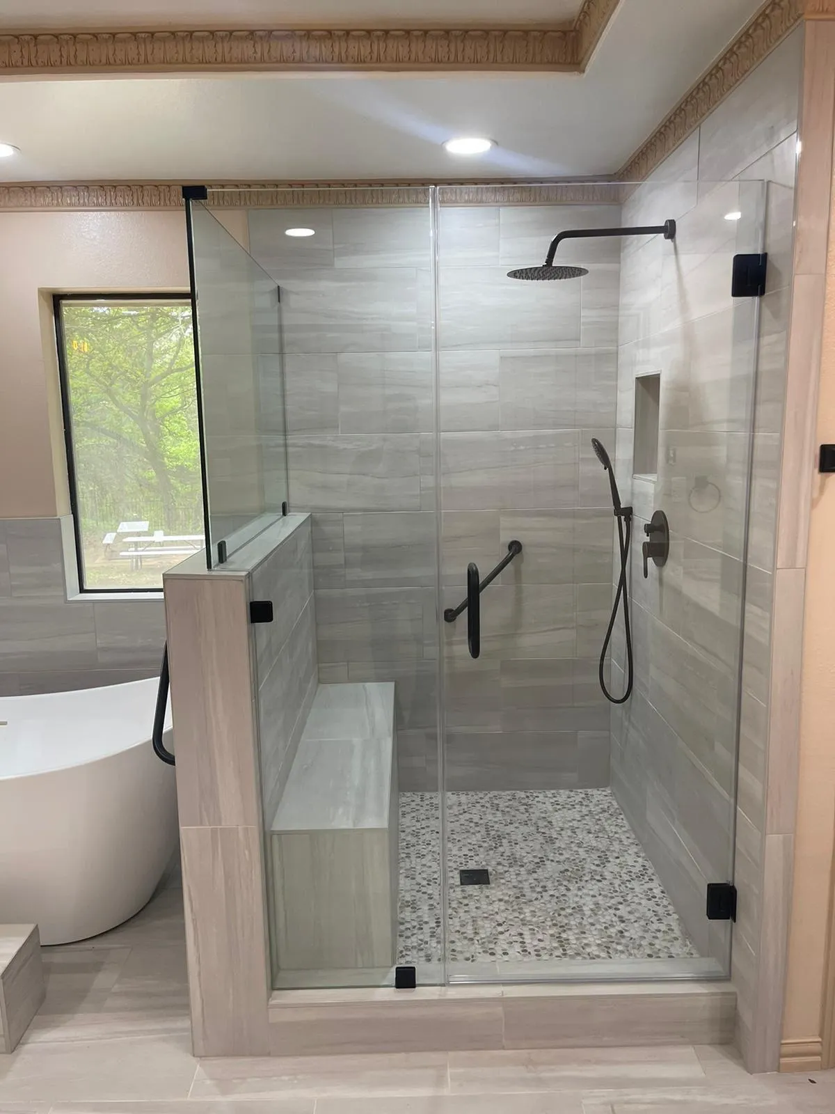 Glass walk-in shower with bench next to a freestanding tub