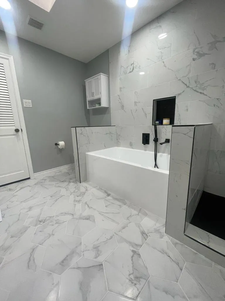 Marble-look tile walls and soaking tub with black faucet, Dallas bathroom remodel