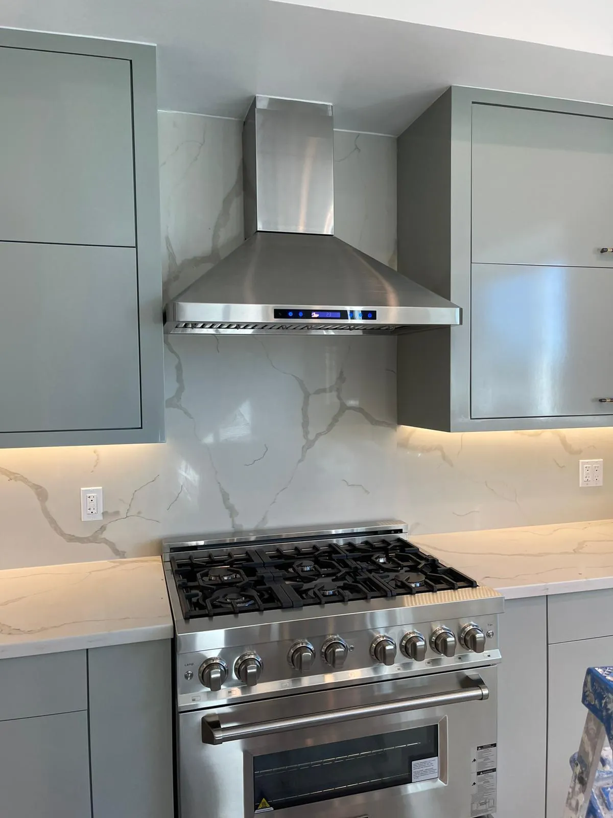 Range wall with quartz slab backsplash and chimney hood